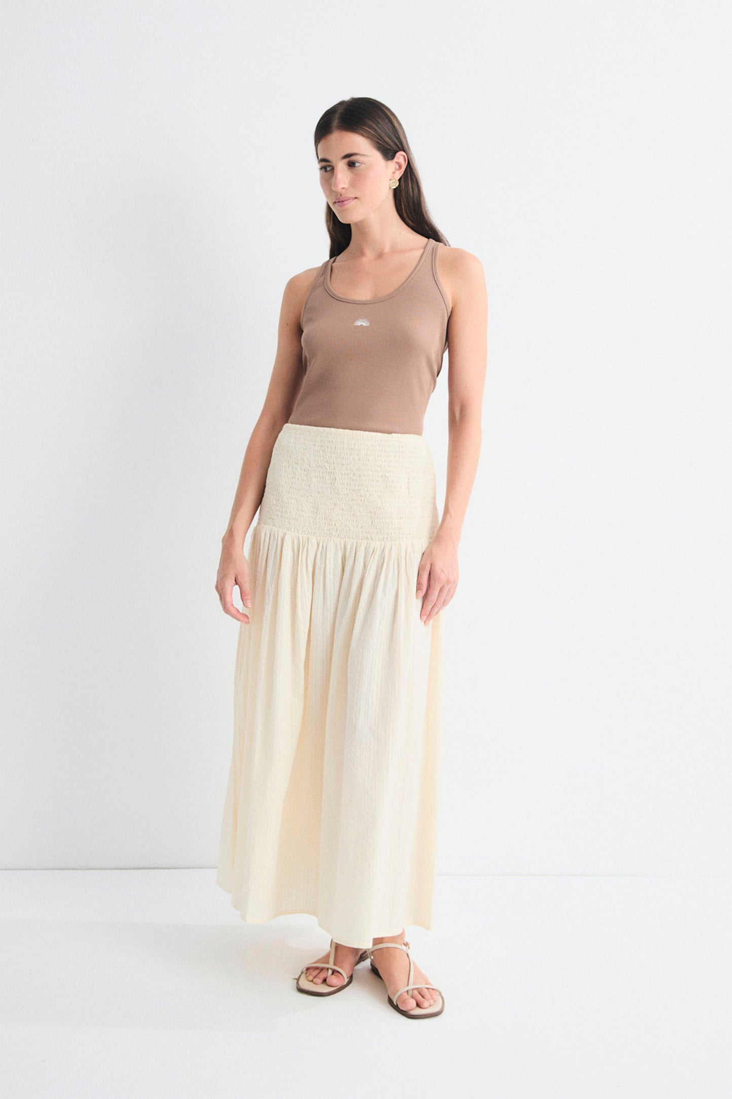 Woman wearing a beige tank top and long cream skirt on a white background