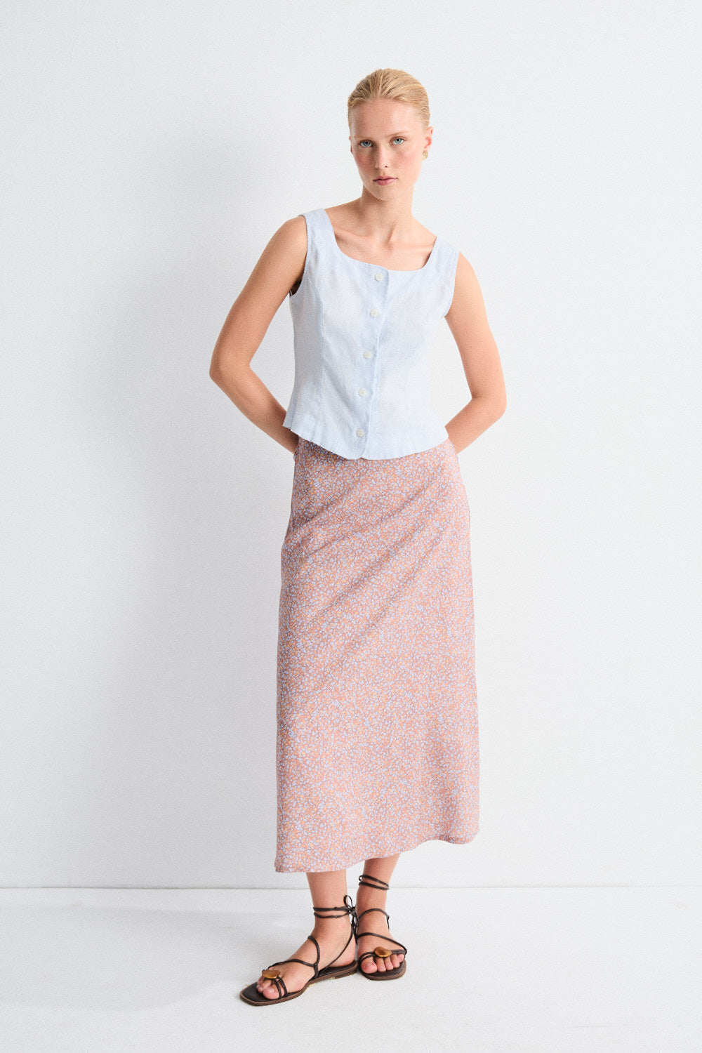 Woman wearing a light blue sleeveless top and pink skirt against a white background