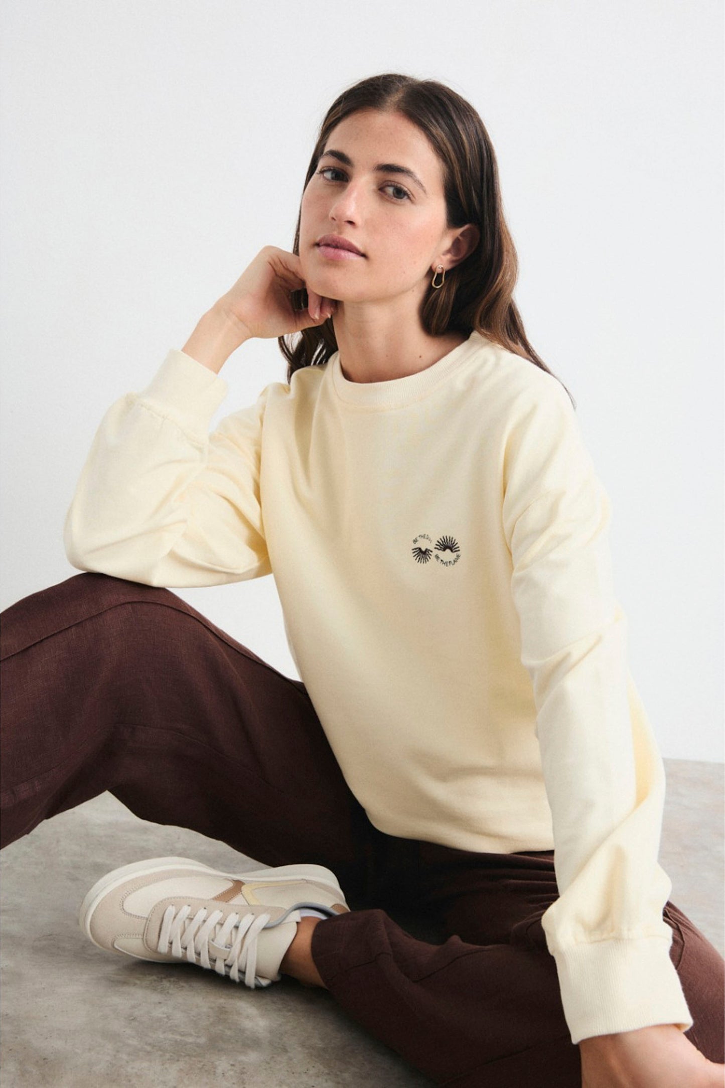 Woman wearing a light yellow sweatshirt with a small graphic on a plain background