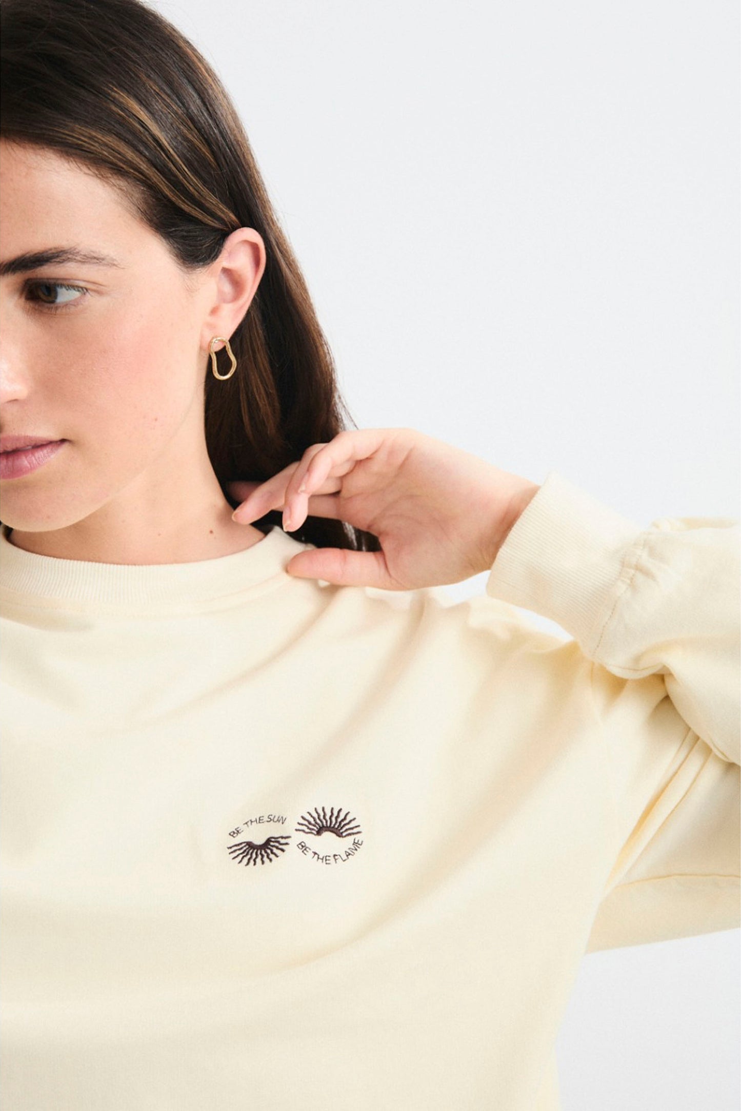 Woman wearing a light yellow sweatshirt with a logo on a white background