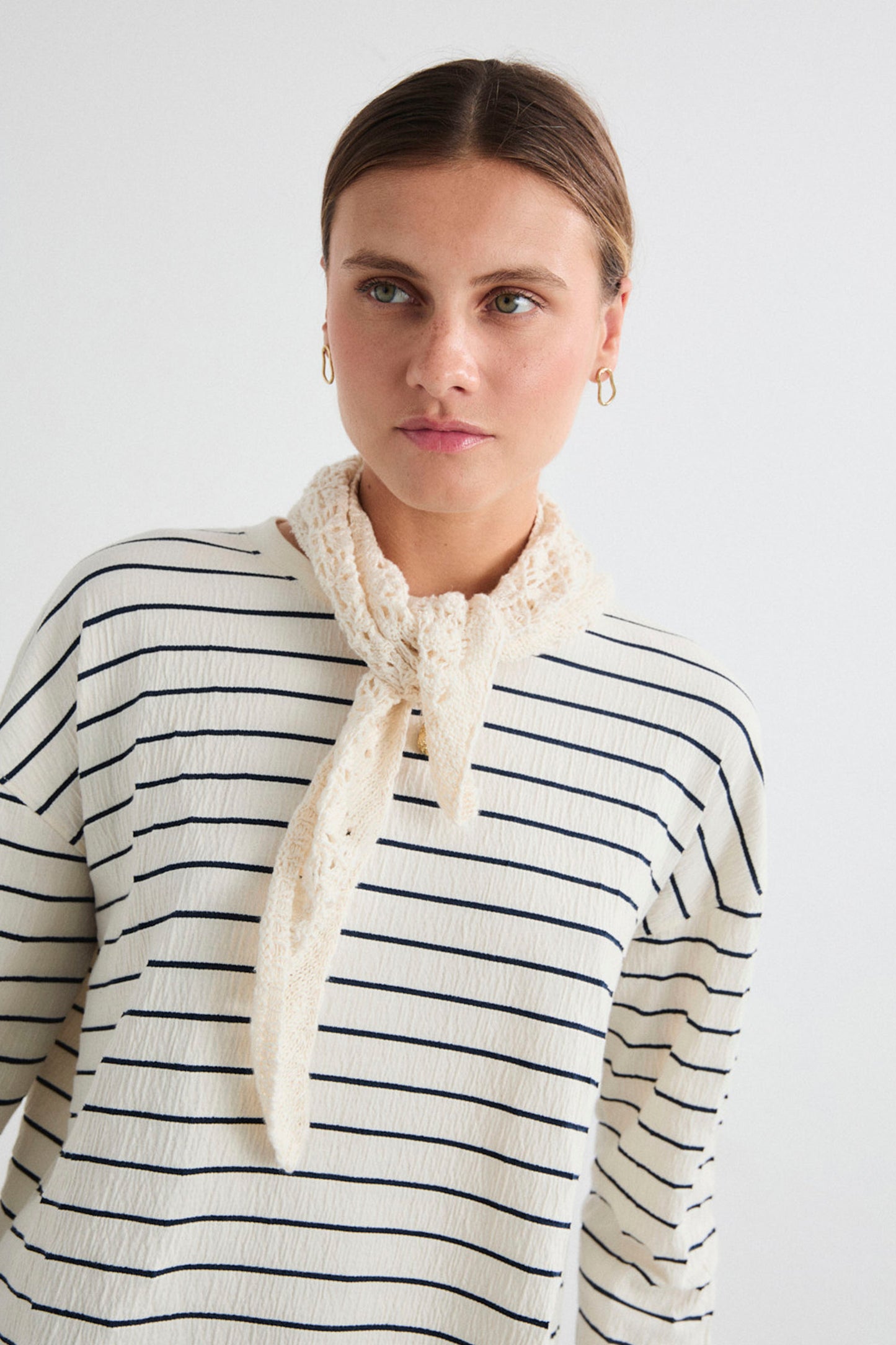 Woman wearing a striped Mus&Bombon Salana sweater with a scarf against a plain background