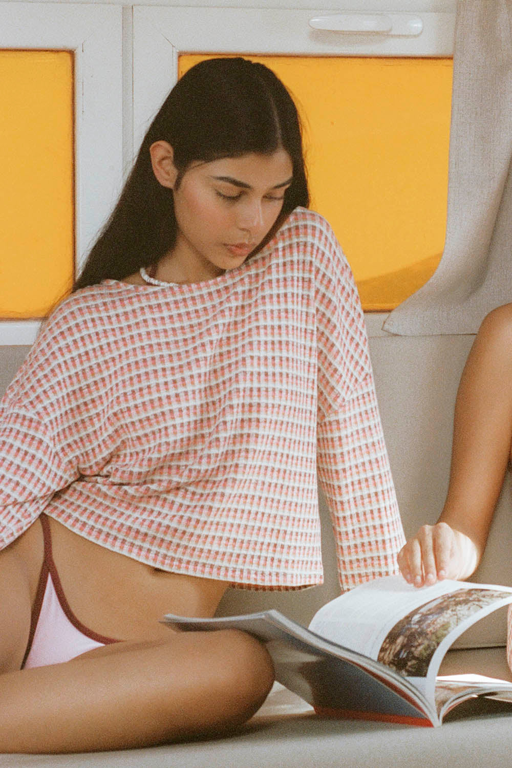 Woman reading a magazine on a couch with yellow walls in the background