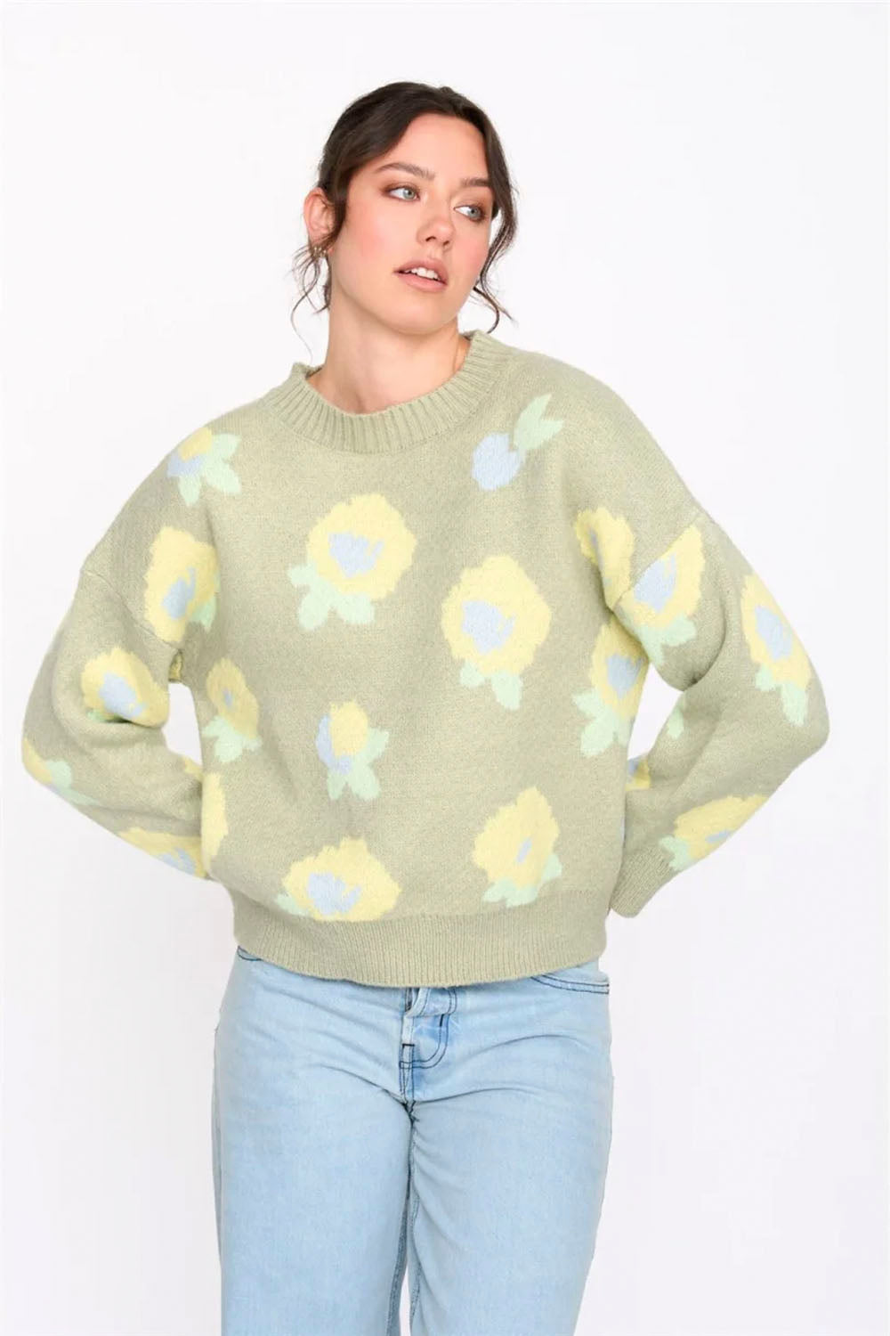 Woman wearing a light green sweater with floral patterns on a white background