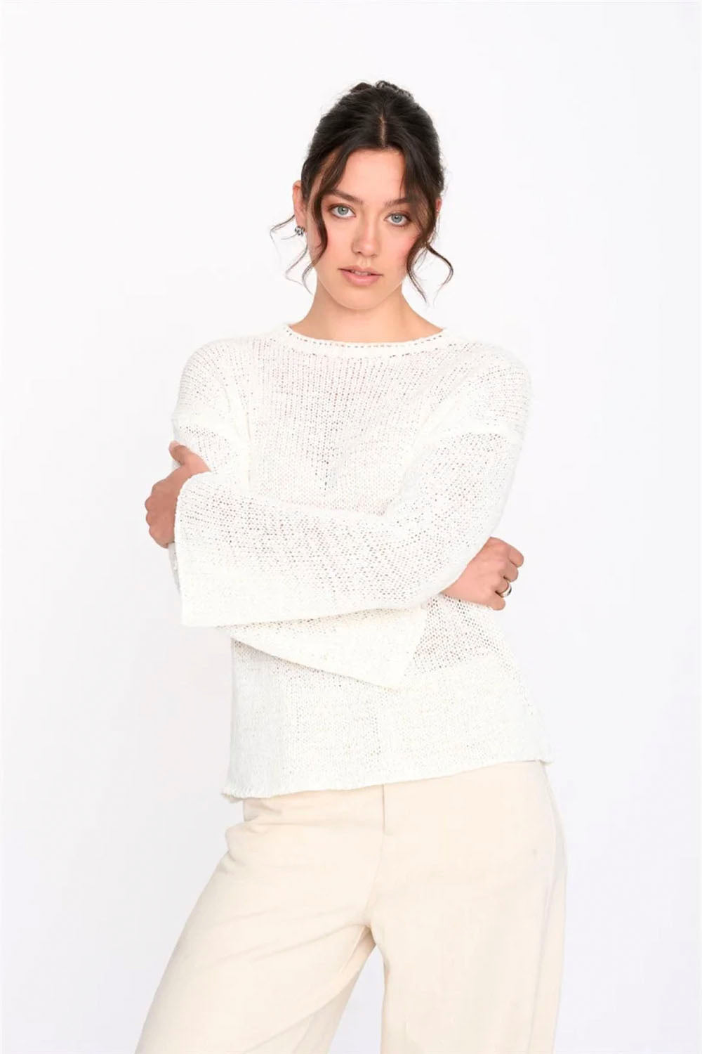 Woman wearing a white textured sweater and cream pants against a white background