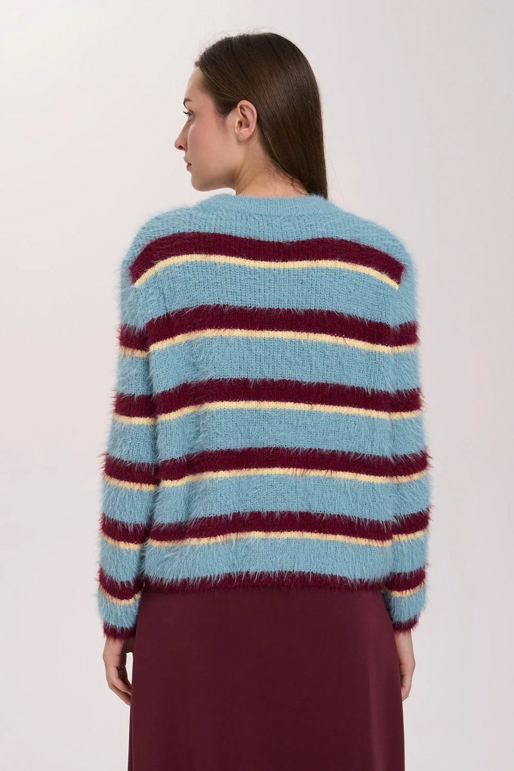A woman shown from the back wearing a fuzzy striped sweater with horizontal bands of light blue, burgundy, and cream, paired with a solid burgundy skirt against a plain light gray studio background.