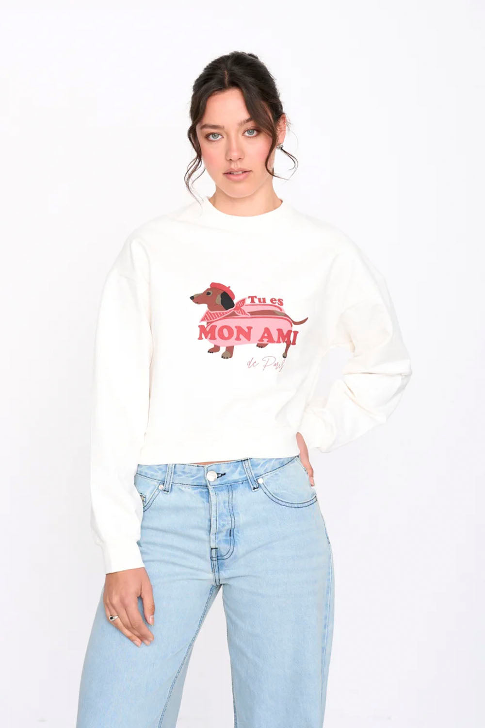 Person wearing a white sweatshirt with a graphic design and light blue jeans on a white background