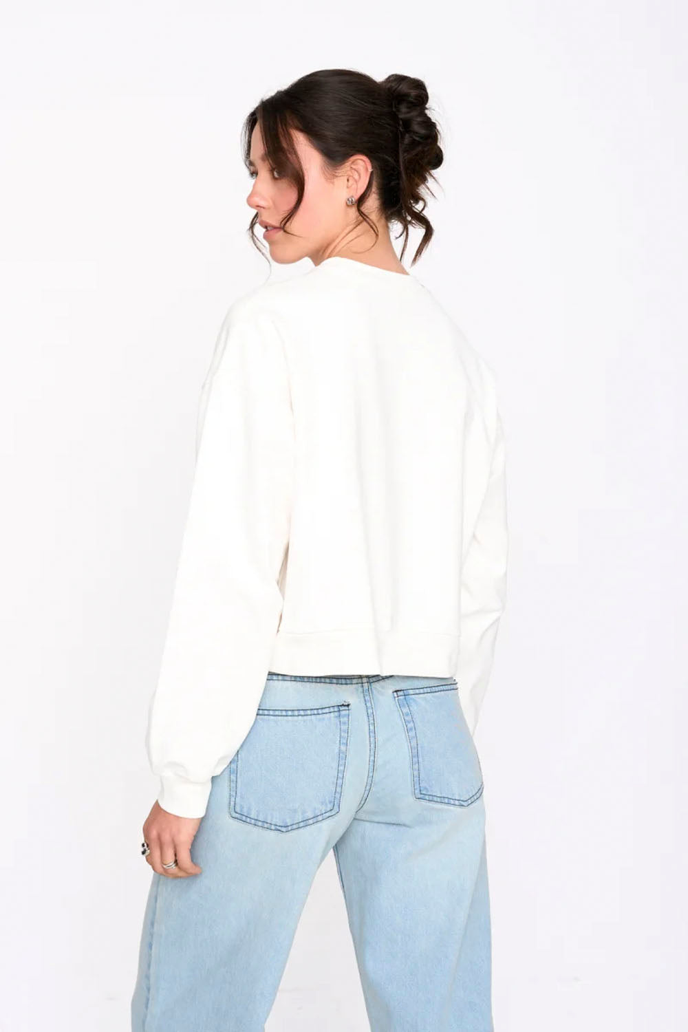 Woman wearing a white long-sleeve shirt and light blue jeans on a white background