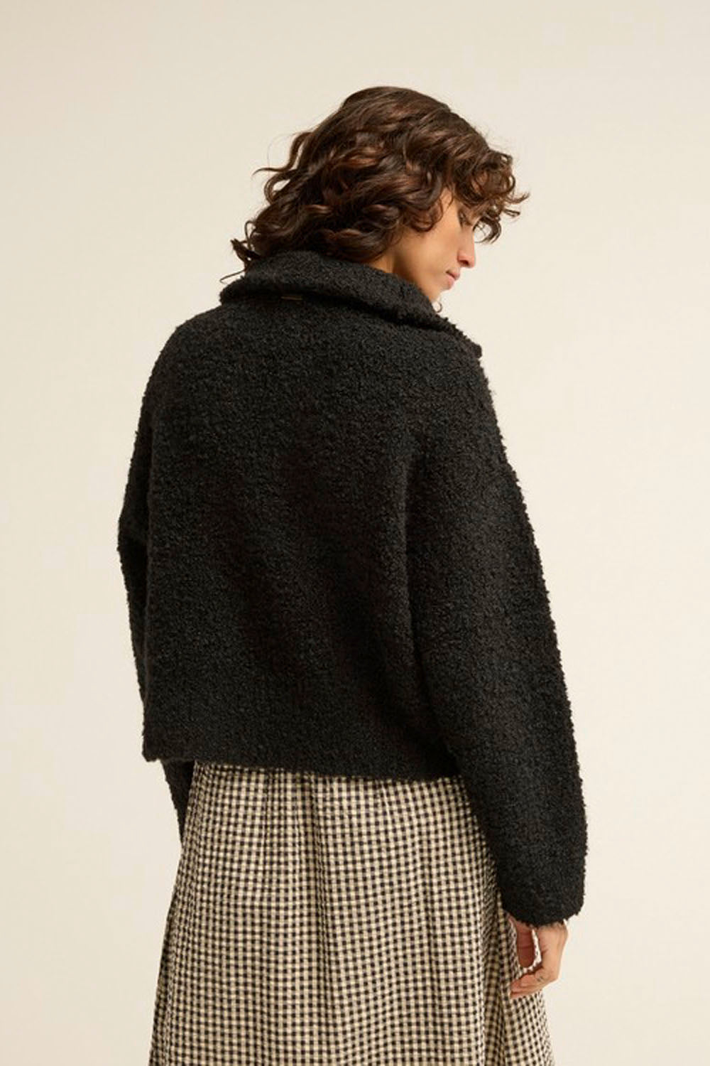 A model shown from the back wearing a black fuzzy cropped jacket and a beige and black houndstooth skirt, set against a plain off-white background.
