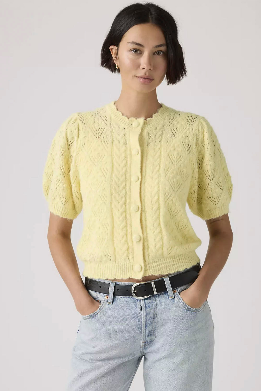 Woman wearing a yellow knitted cardigan and light blue jeans on a plain background