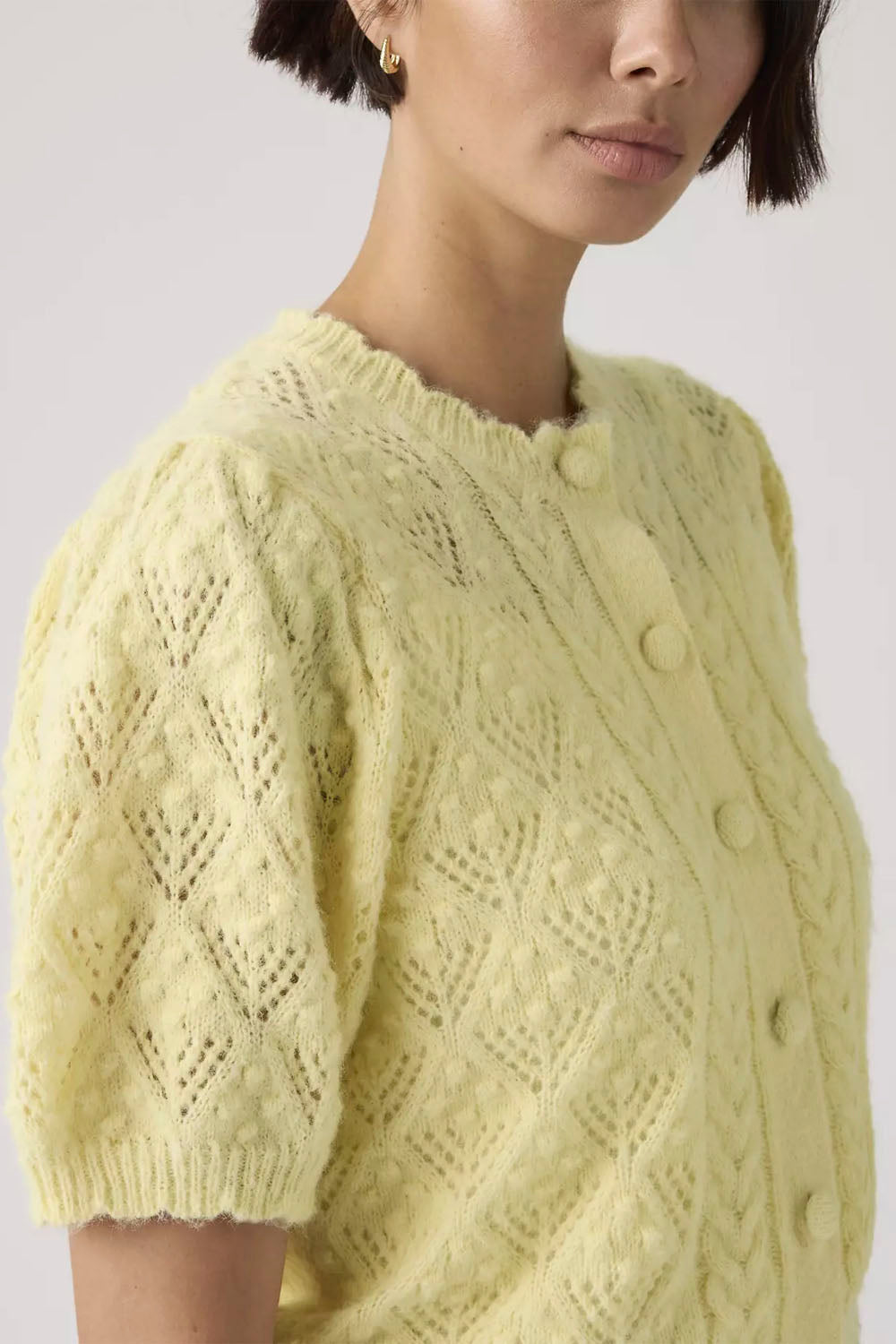 Person wearing a light yellow knitted cardigan with a textured pattern on a plain background