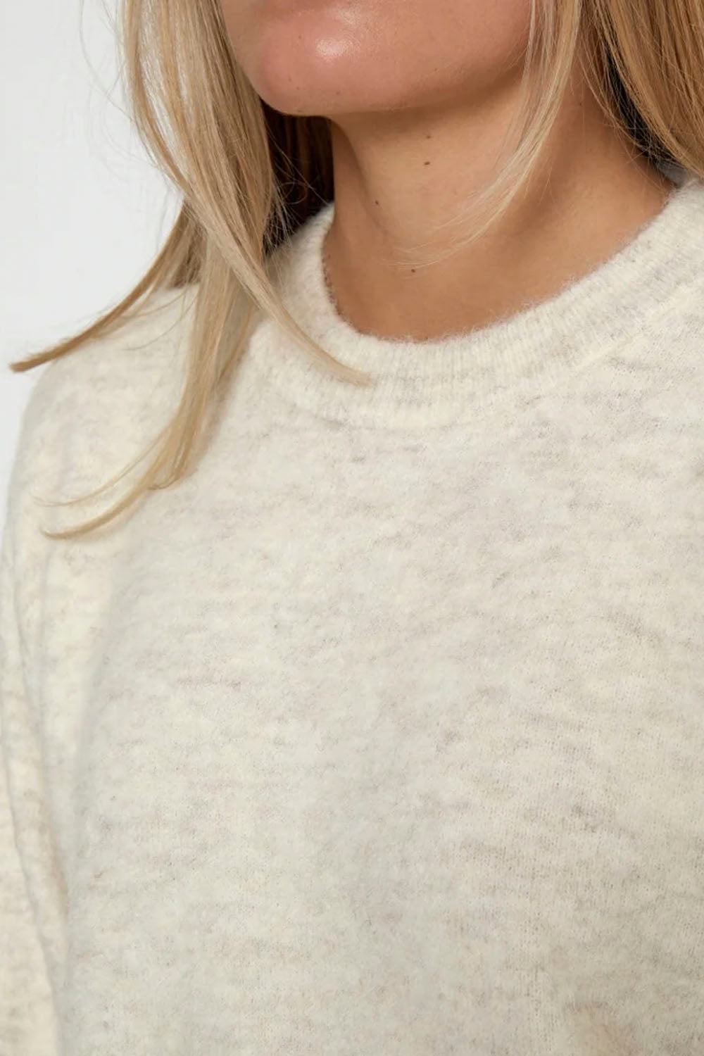 Close-up of a person wearing a soft, heathered cream knit sweater, showing the texture of the fabric and the collar against a plain light background.