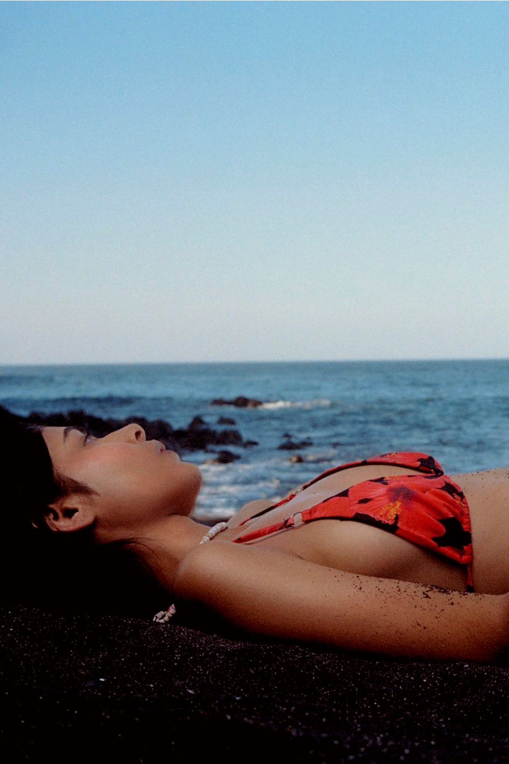 Person lying on a beach wearing a red bikini with a clear sky and ocean in the background