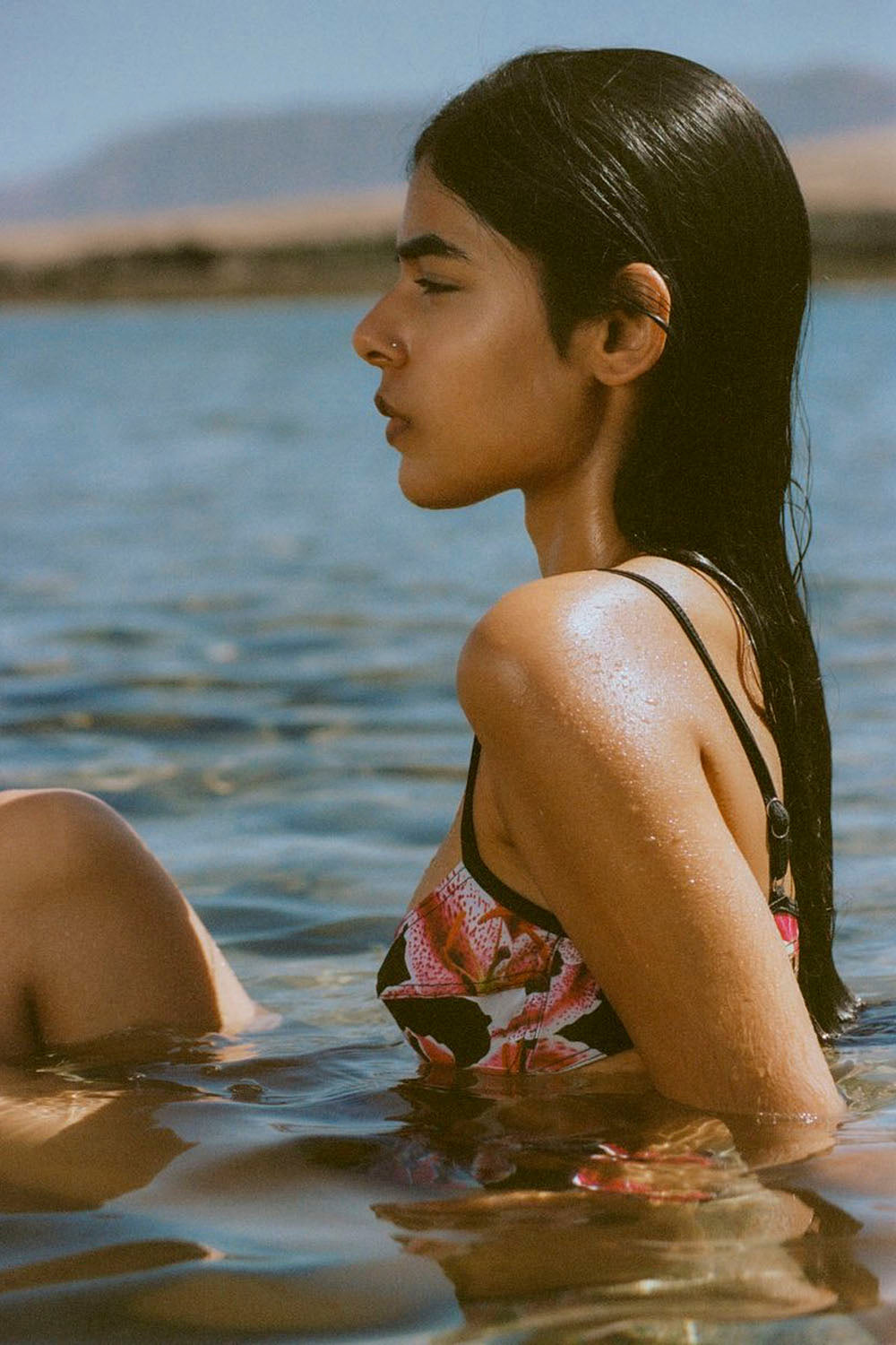 Woman in a floral bikini sitting in water with mountains in the background