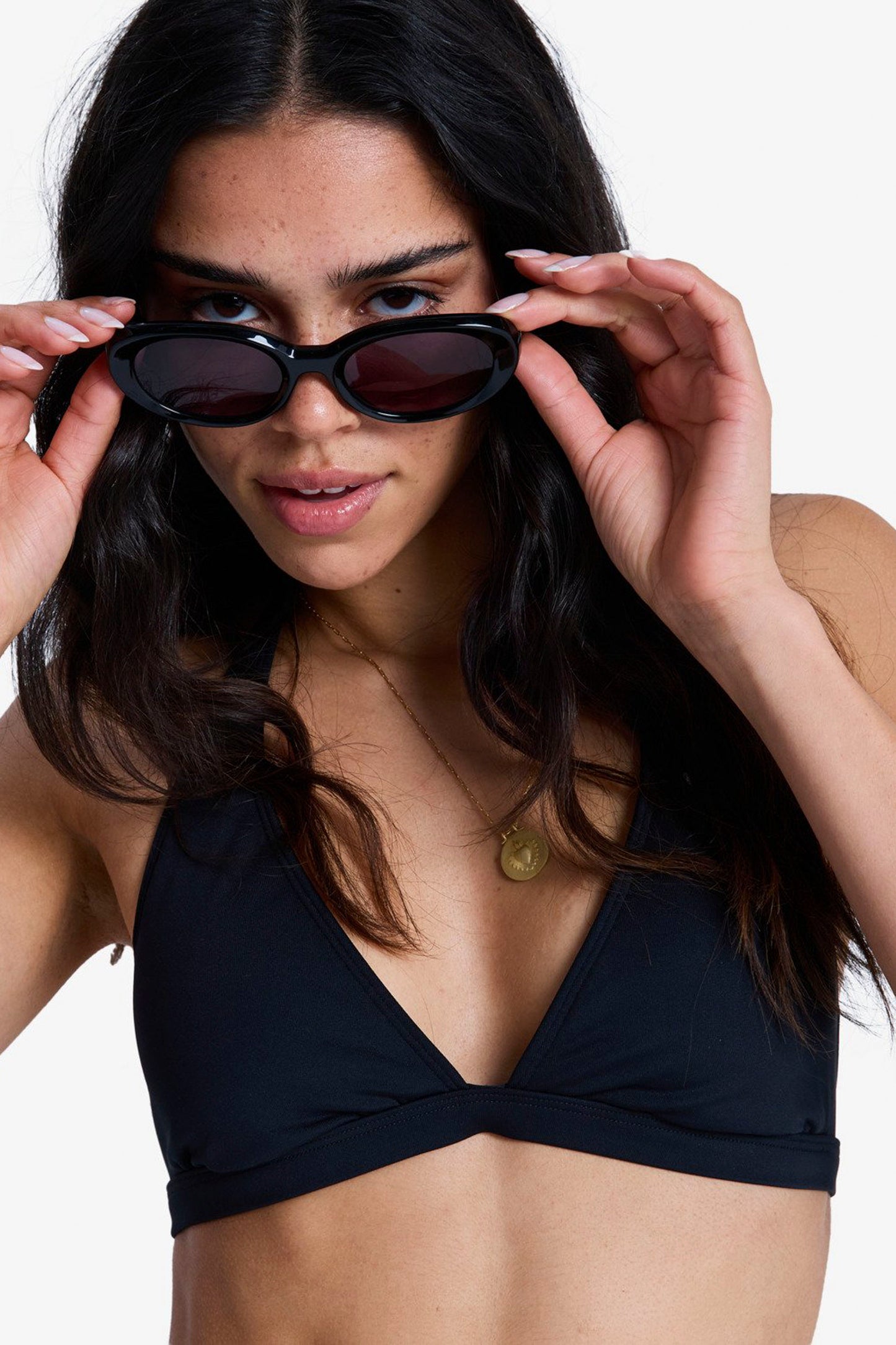 Woman wearing a black bikini top holding sunglasses against a white background