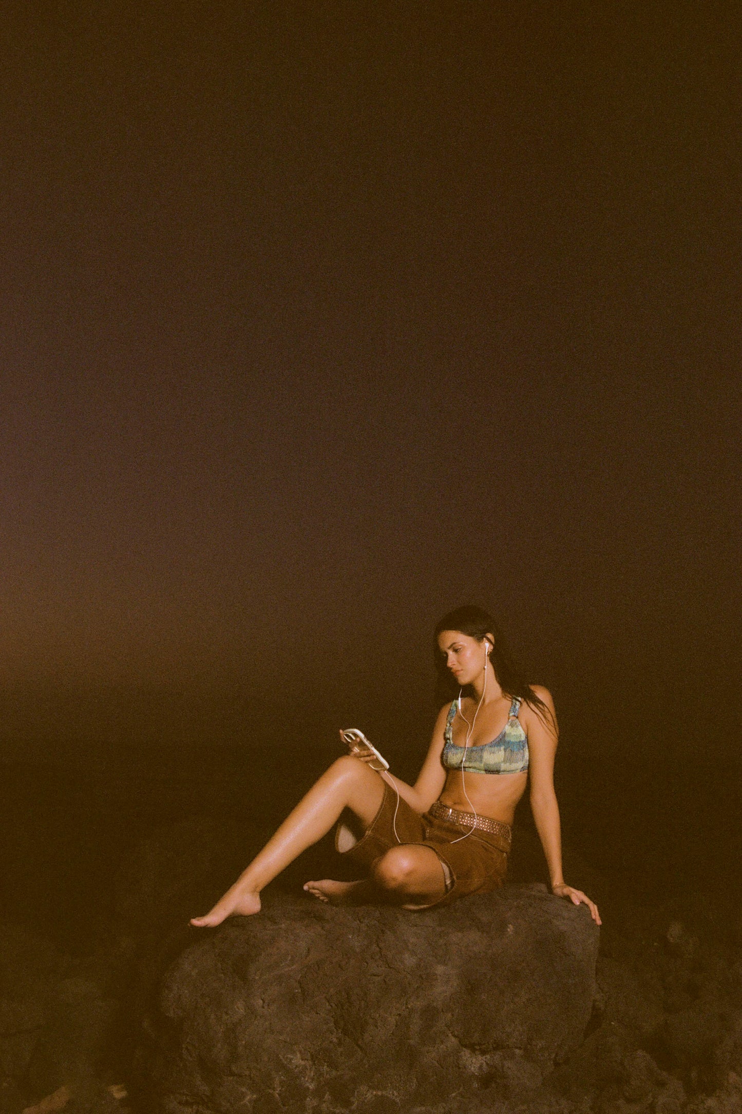 Woman sitting on a rock at dusk, using a phone.