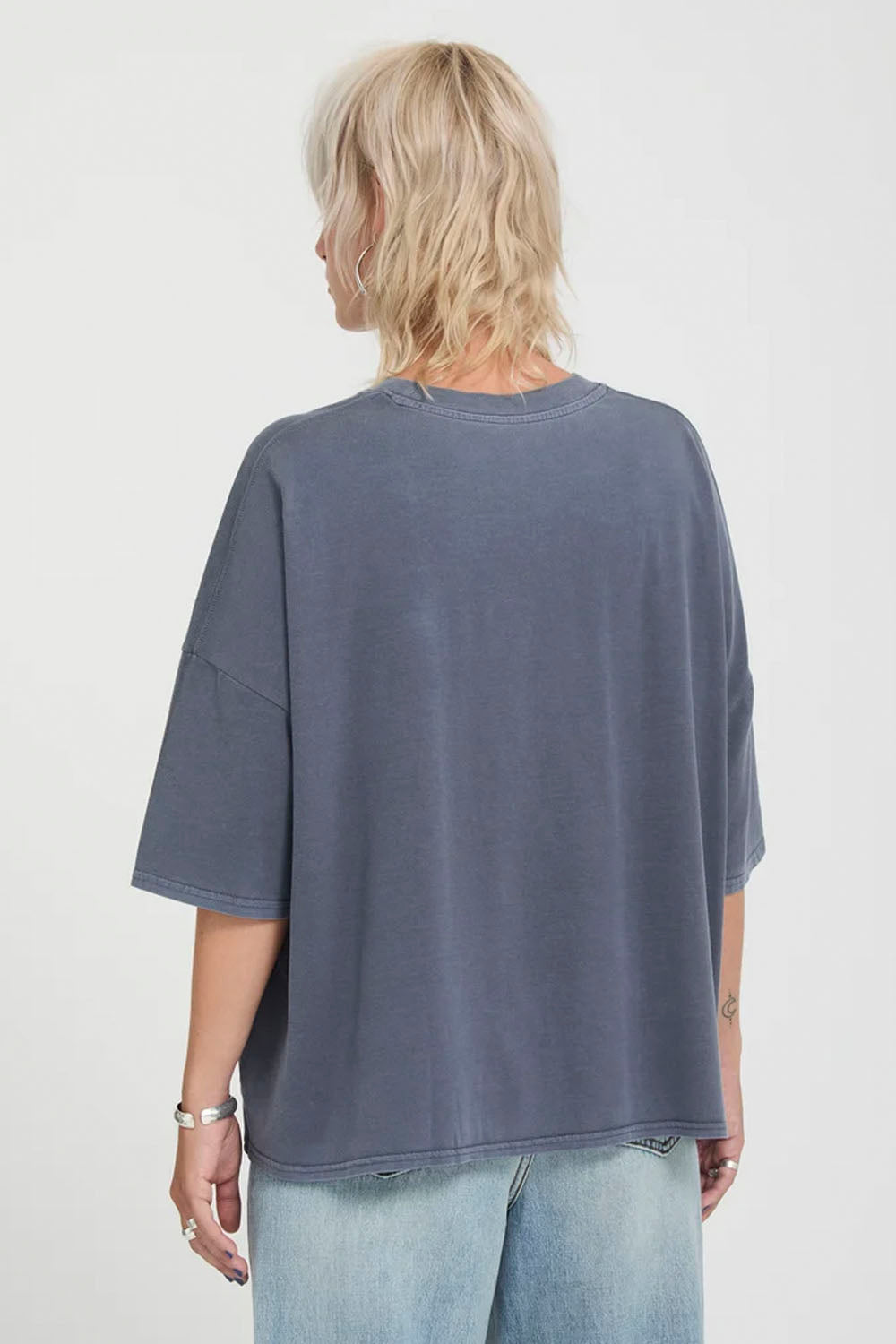 A person shown from the back wearing an oversized washed slate blue t-shirt and light blue jeans against a plain white background.