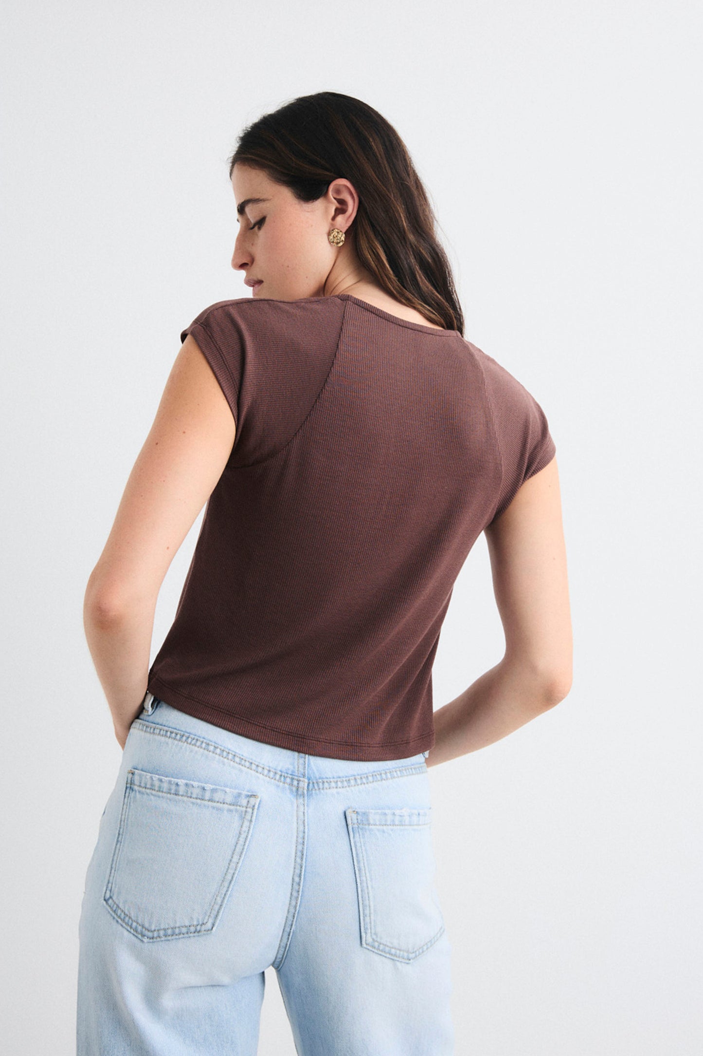 Woman wearing a brown sleeveless top and light blue jeans on a white background