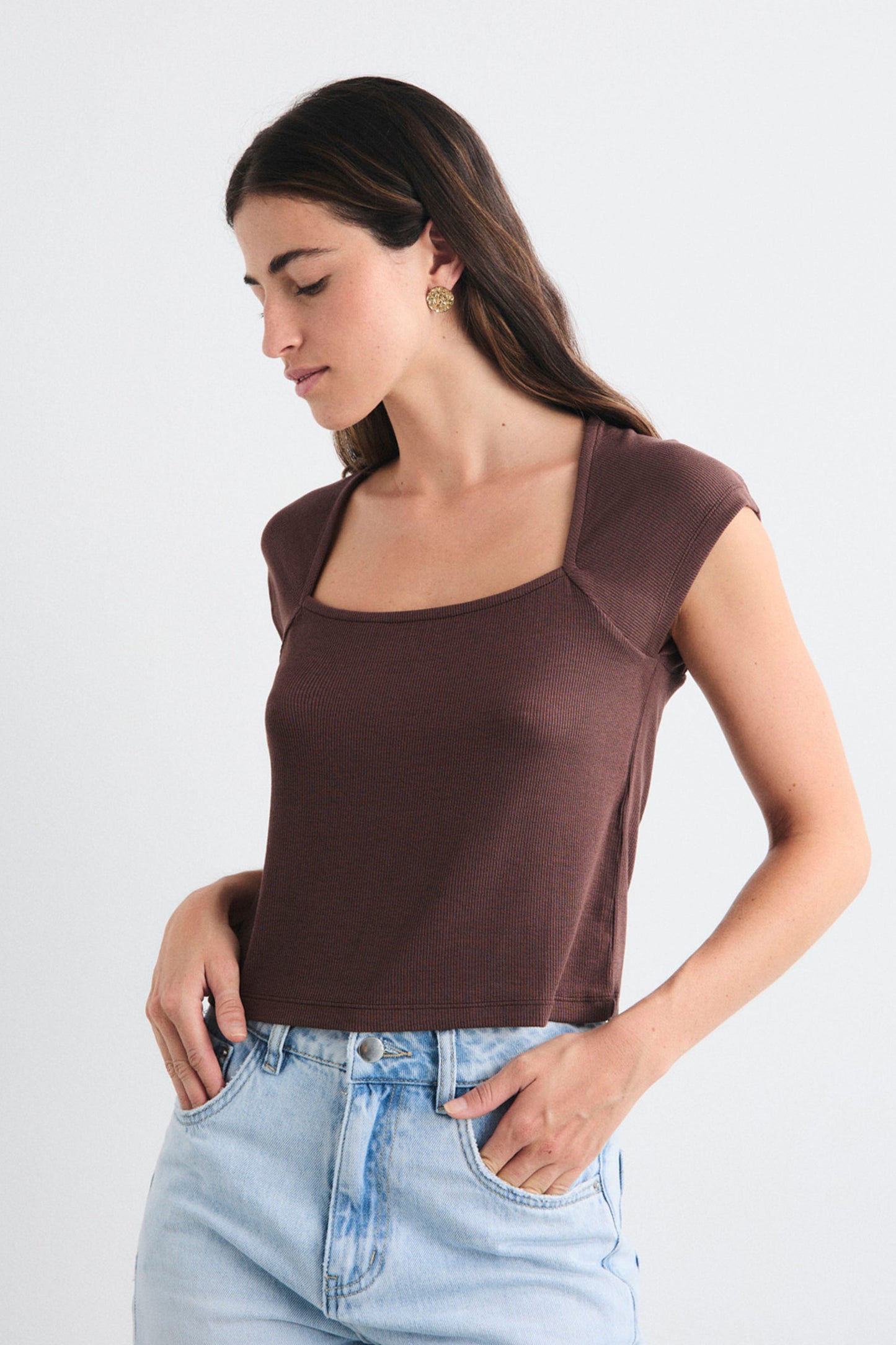 Woman wearing a brown top and light blue jeans on a white background