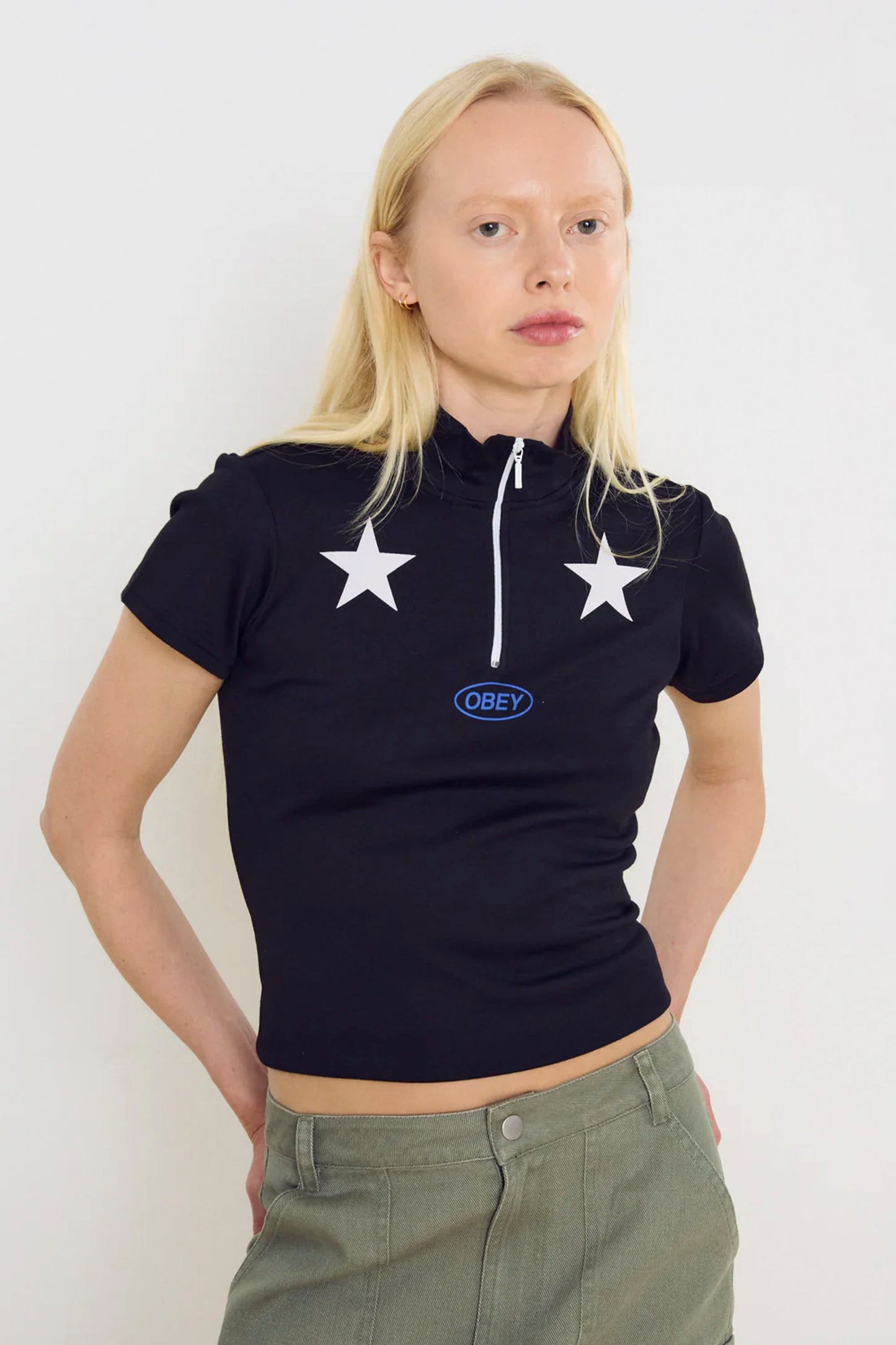 Person wearing a black OBEY Relay Mock Neck T-Shirt with star designs and an 'Obey' logo, standing against a white background.