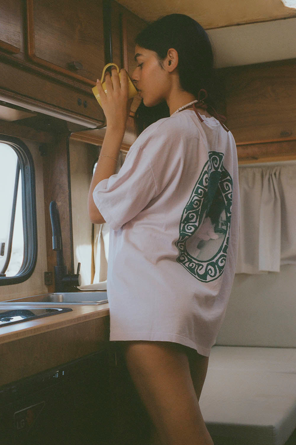 Person drinking from a cup inside a vehicle, wearing a white t-shirt with a green logo.