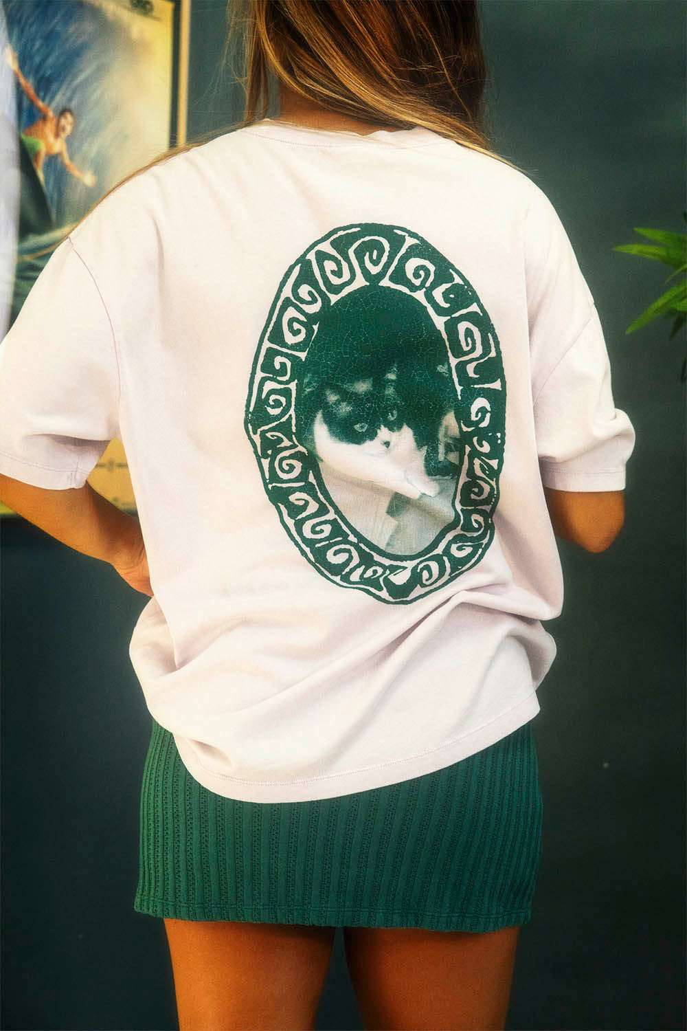 Person wearing a white t-shirt with a cat graphic on the back, standing against a dark background.