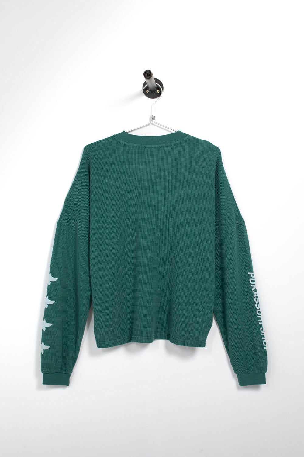 A dark green long-sleeve crewneck sweatshirt hanging on a white hanger against a white wall. The left sleeve features a vertical white text graphic reading 'PULSARSCOUT.
