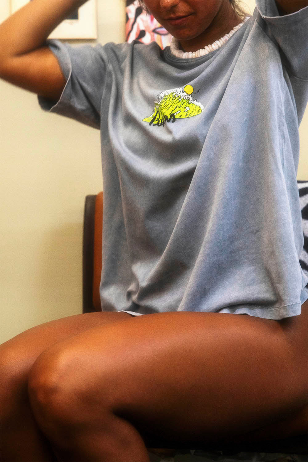 Person wearing a light blue t-shirt with a graphic design, sitting on a chair.