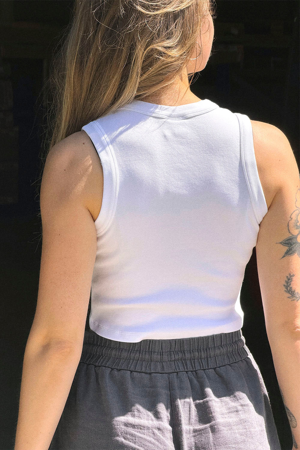 Person wearing a white sleeveless top with a dark background