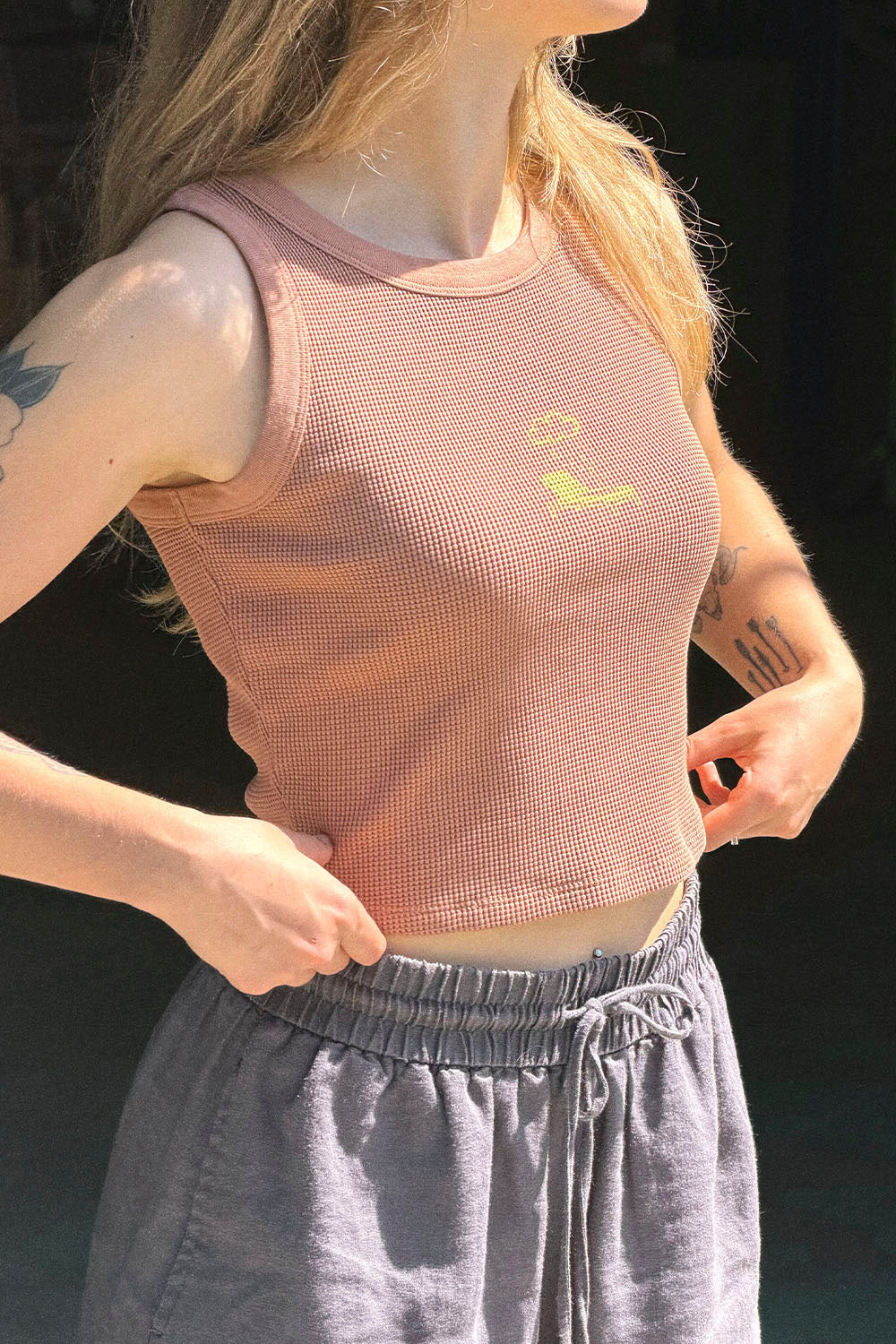 Person wearing a pink mesh tank top with a small design on a black background