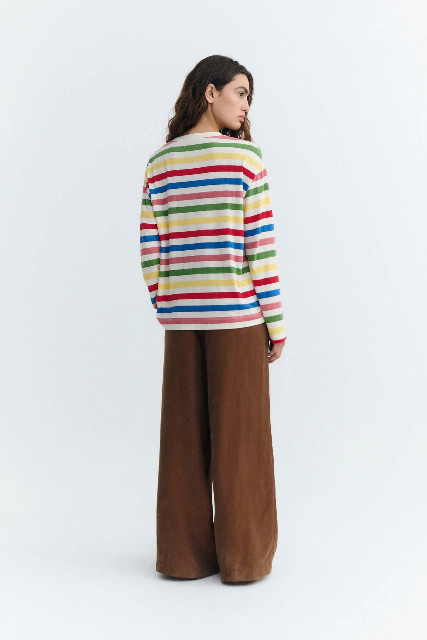 Person wearing a colorful striped Thinking Mu sweater and brown pants on a white background