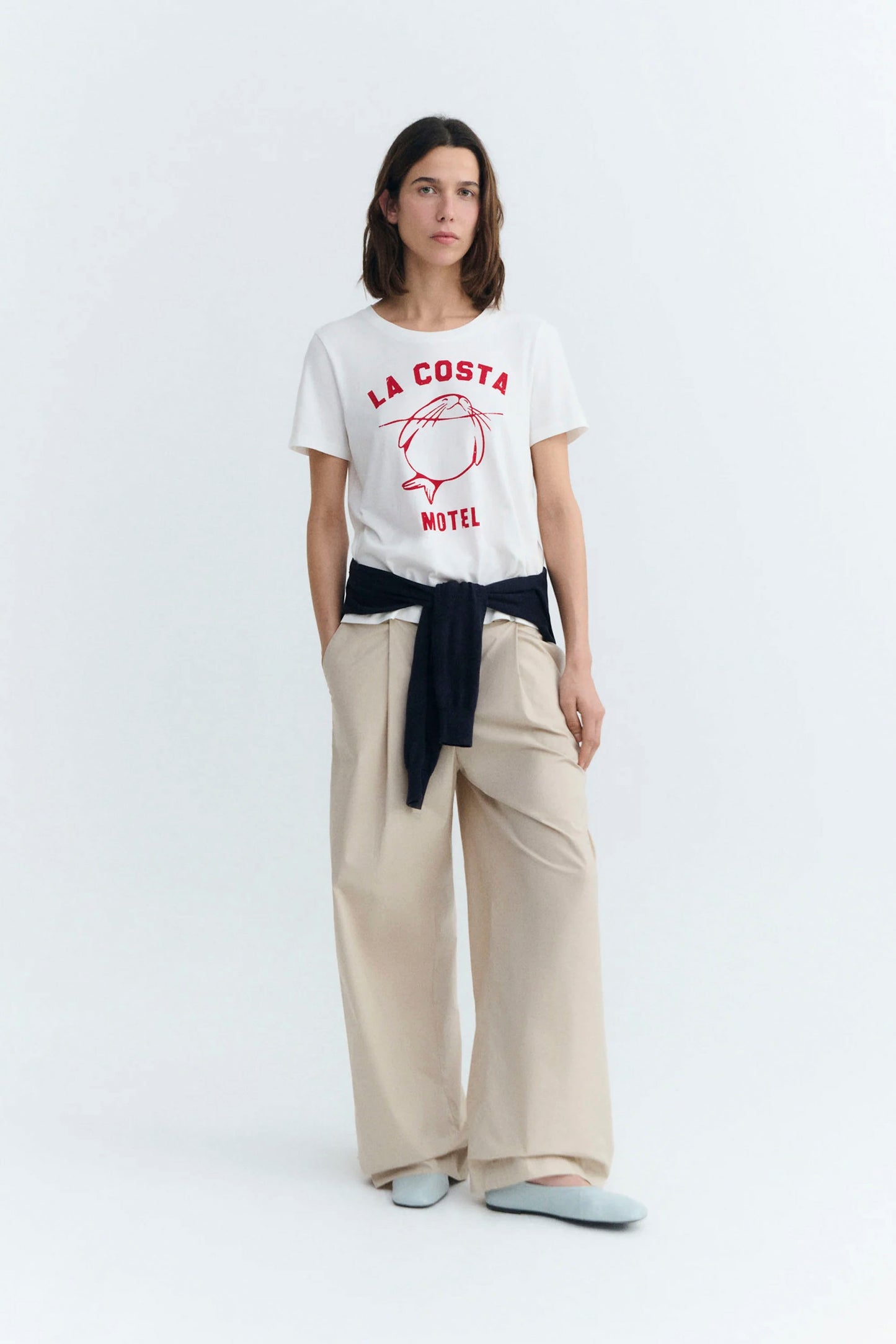 Person wearing a white Thinking Mu t-shirtwith red graphics and text, beige pants, and gray shoes on a white background