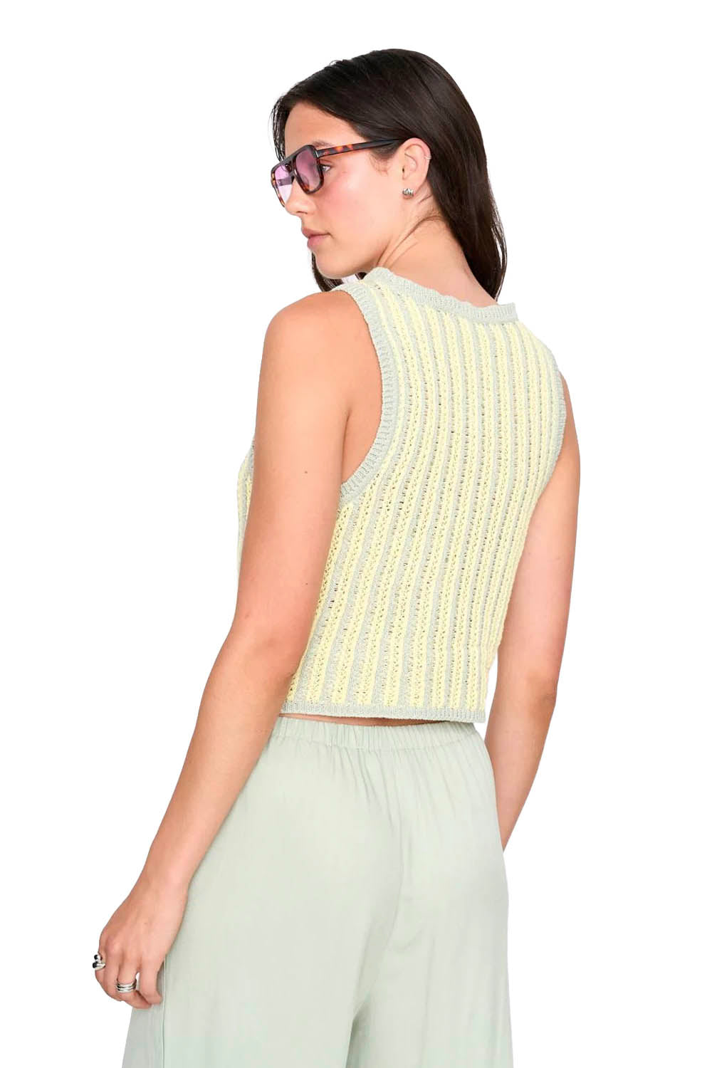 Woman wearing a light green sleeveless top and light gray pants on a white background