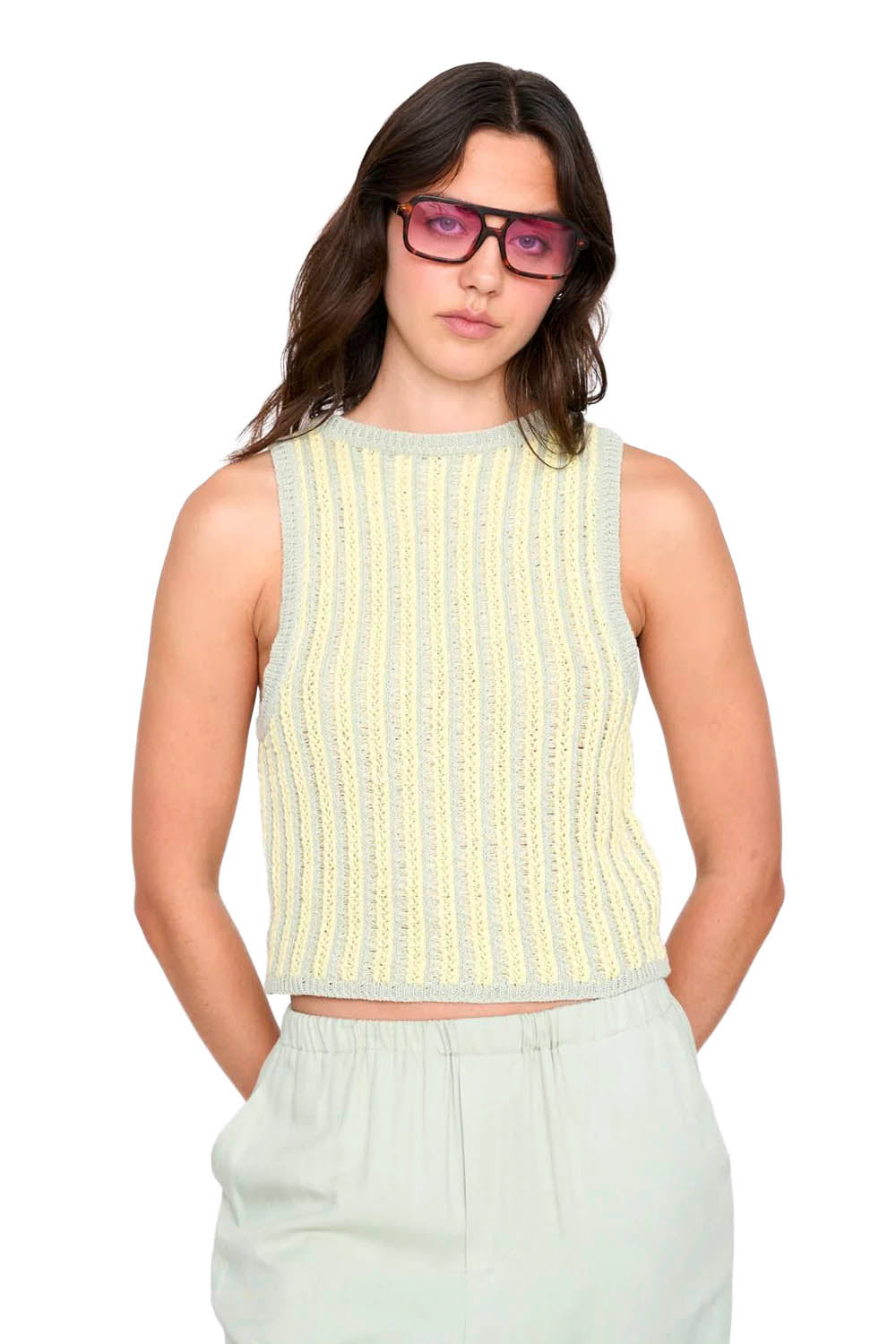 Woman wearing a yellow sleeveless top and light pants on a white background