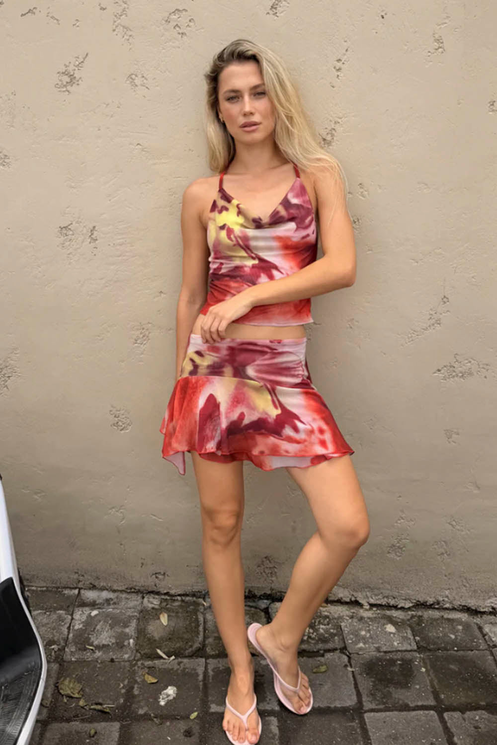 Woman wearing a colorful dress standing against a textured wall.