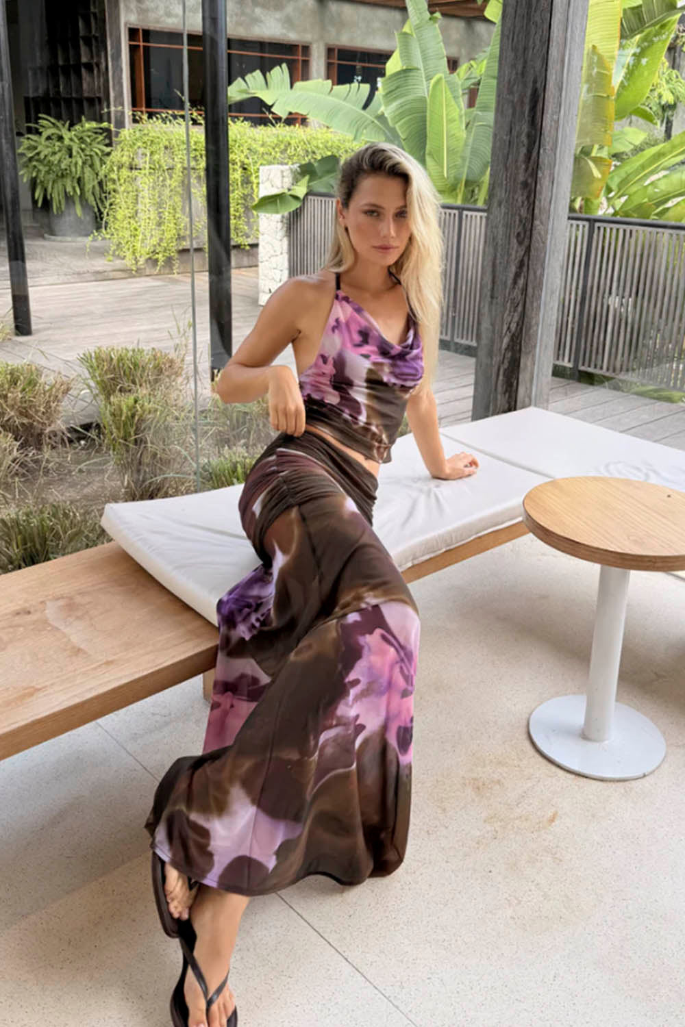 Woman in a tie-dye outfit sitting on a lounge chair outdoors.