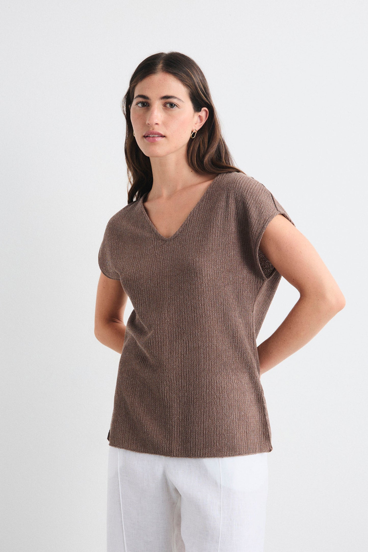 Woman wearing a brown short-sleeve top and white pants on a light gray background