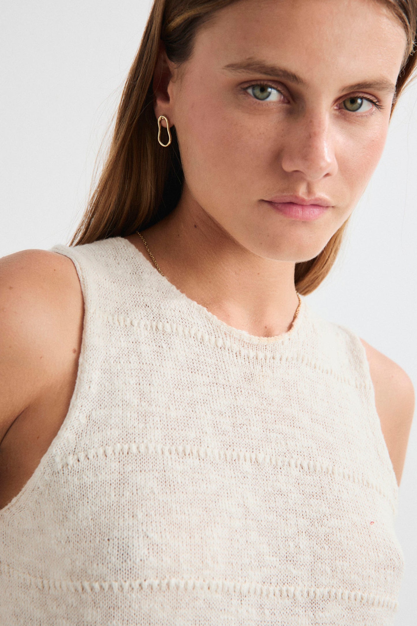 Woman wearing a white sleeveless top against a plain background