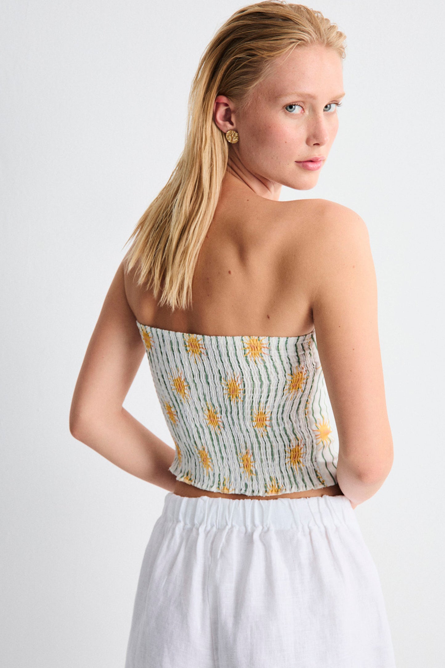 Woman wearing a strapless top with pineapple pattern and white pants on a light gray background