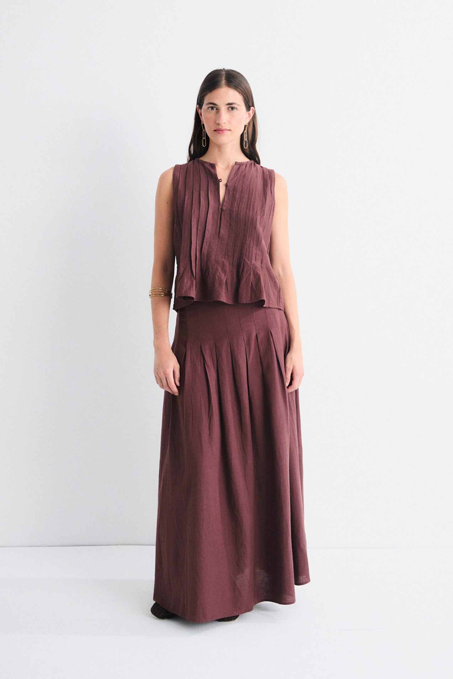 Woman wearing a sleeveless brown top and long skirt on a white background