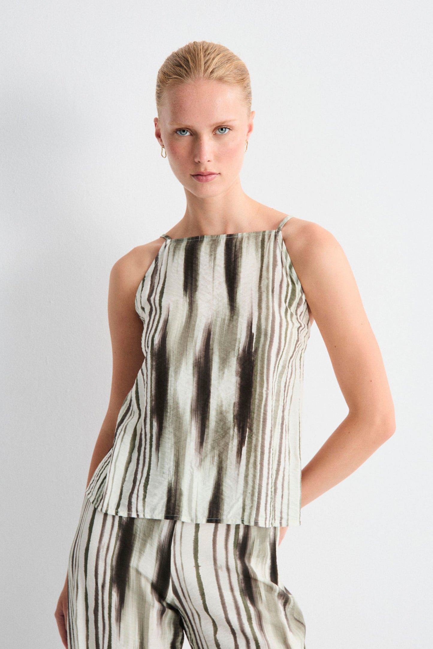 Woman wearing a sleeveless top and pants with a black and white pattern on a light gray background