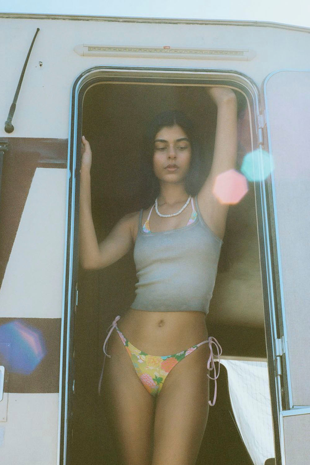 Woman in a bikini standing inside a vehicle with a reflective surface.
