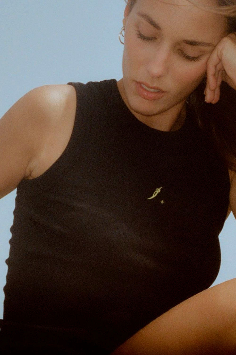 Woman wearing a black sleeveless top with a small yellow detail against a light blue background