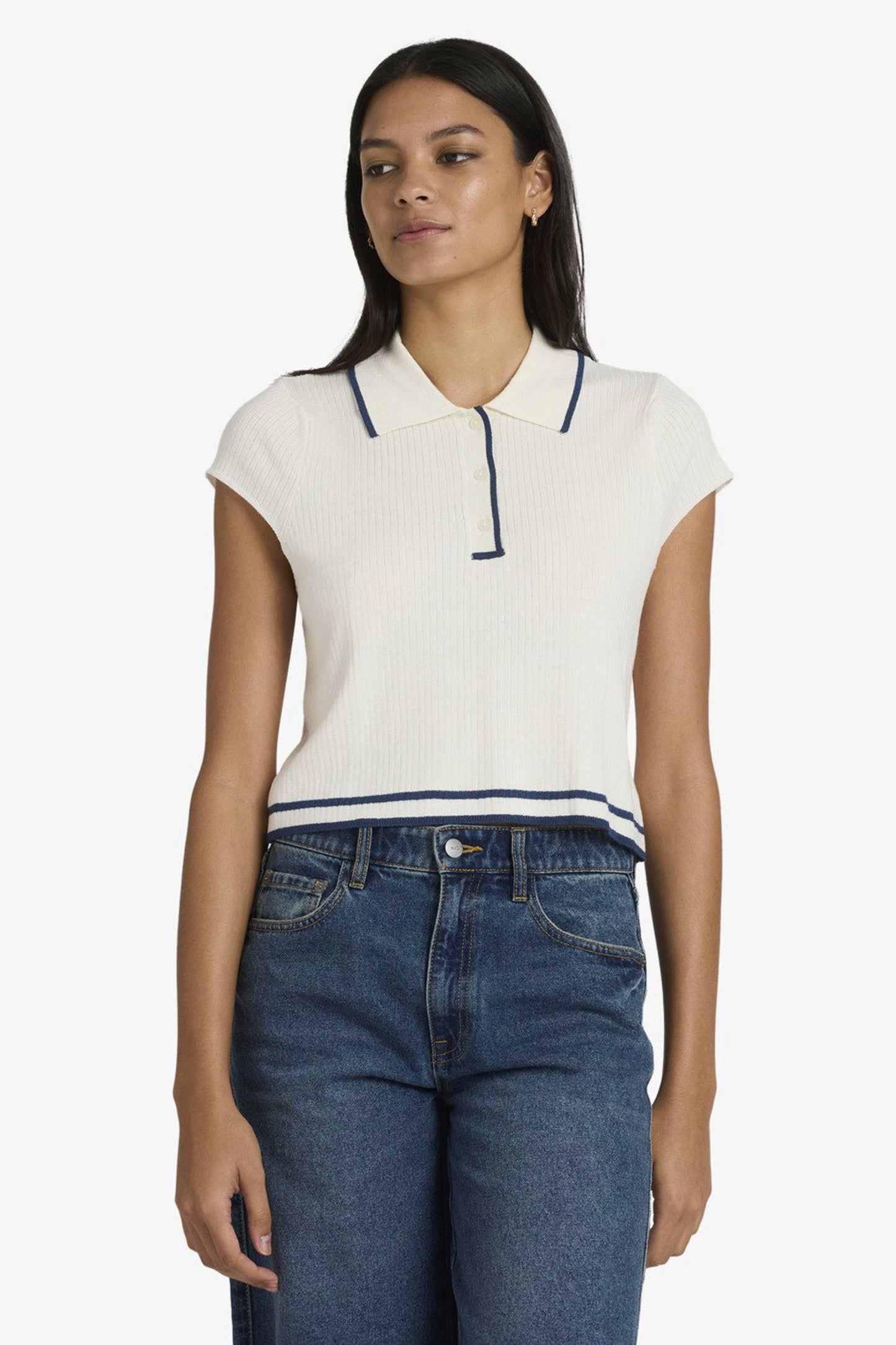 Woman wearing a white RVCA Jules Sweater Top with navy accents and blue jeans on a white background
