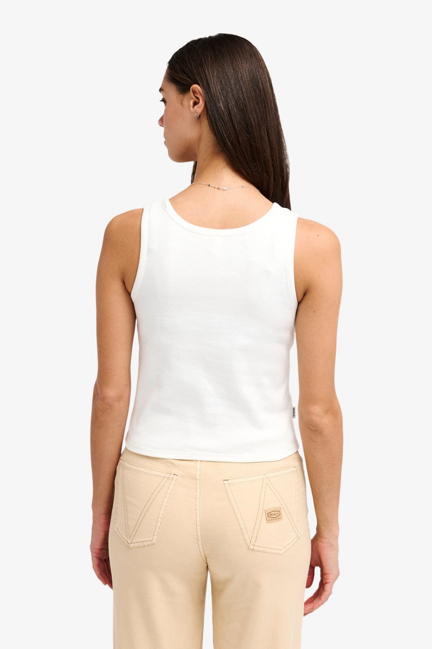 Woman wearing a white RVCA Smiley Tank top and beige pants on a white background