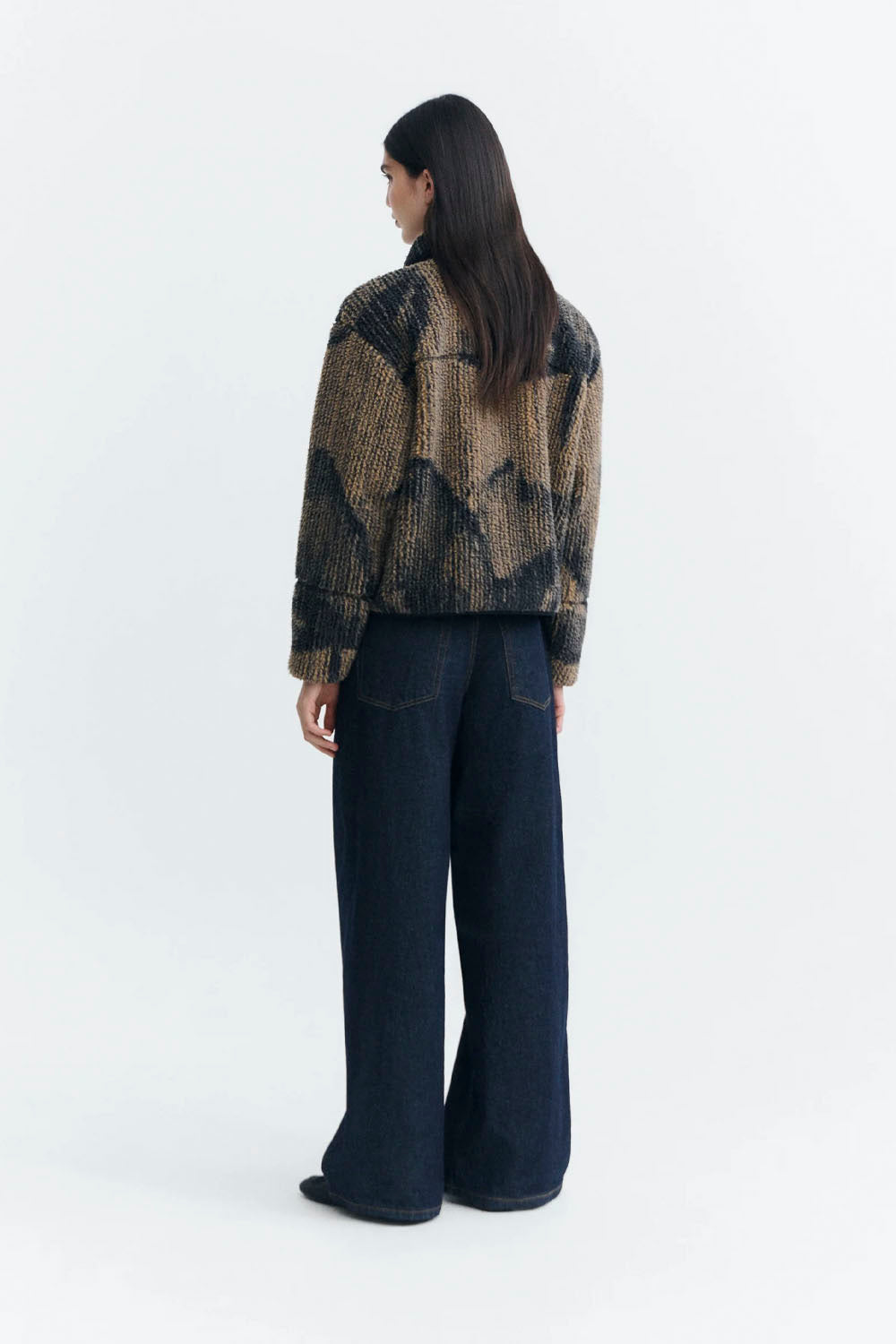 a model wearing a textured, fuzzy zip-up jacket in a brown and black patterned design, with a red shirt visible underneath.
