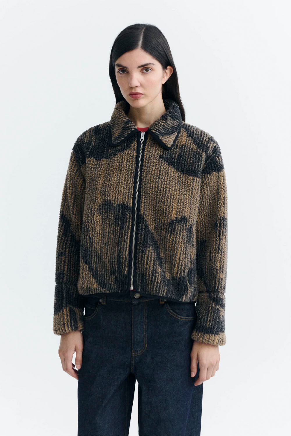 a model wearing a textured, fuzzy zip-up jacket in a brown and black patterned design, with a red shirt visible underneath.