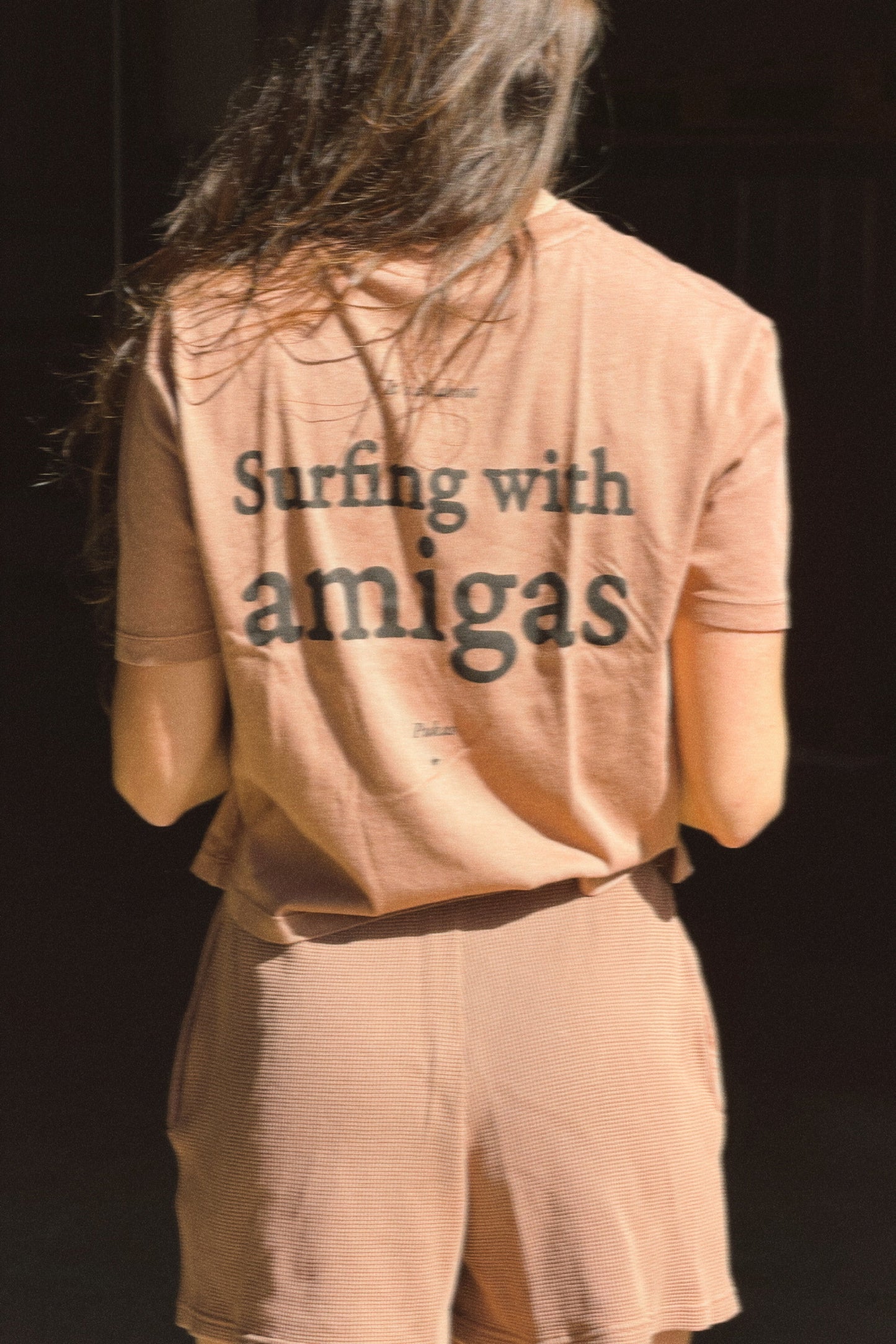 Person wearing a shirt with 'Surfing with amigas' text on a dark background