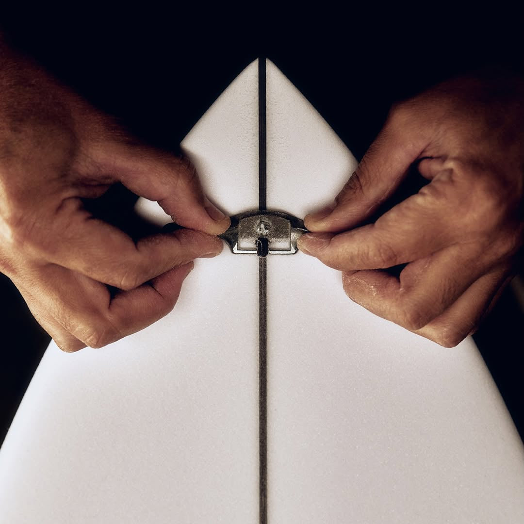 Close-up of hands securing a fin to a white surfboard against a black background